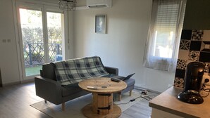 A modern living room with a grey sofa, a round wooden coffee table, and a laptop on a grey ottoman.