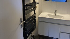 A modern bathroom with a white sink, a mirror with lights, and a black towel rack.
