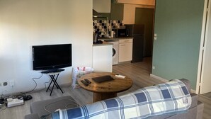 A living room with a flat-screen TV, a sofa, a coffee table, and a kitchen in the background.