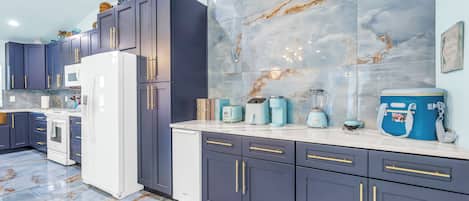 A modern kitchen with dark cabinets, a white refrigerator, and a marble backsplash.
