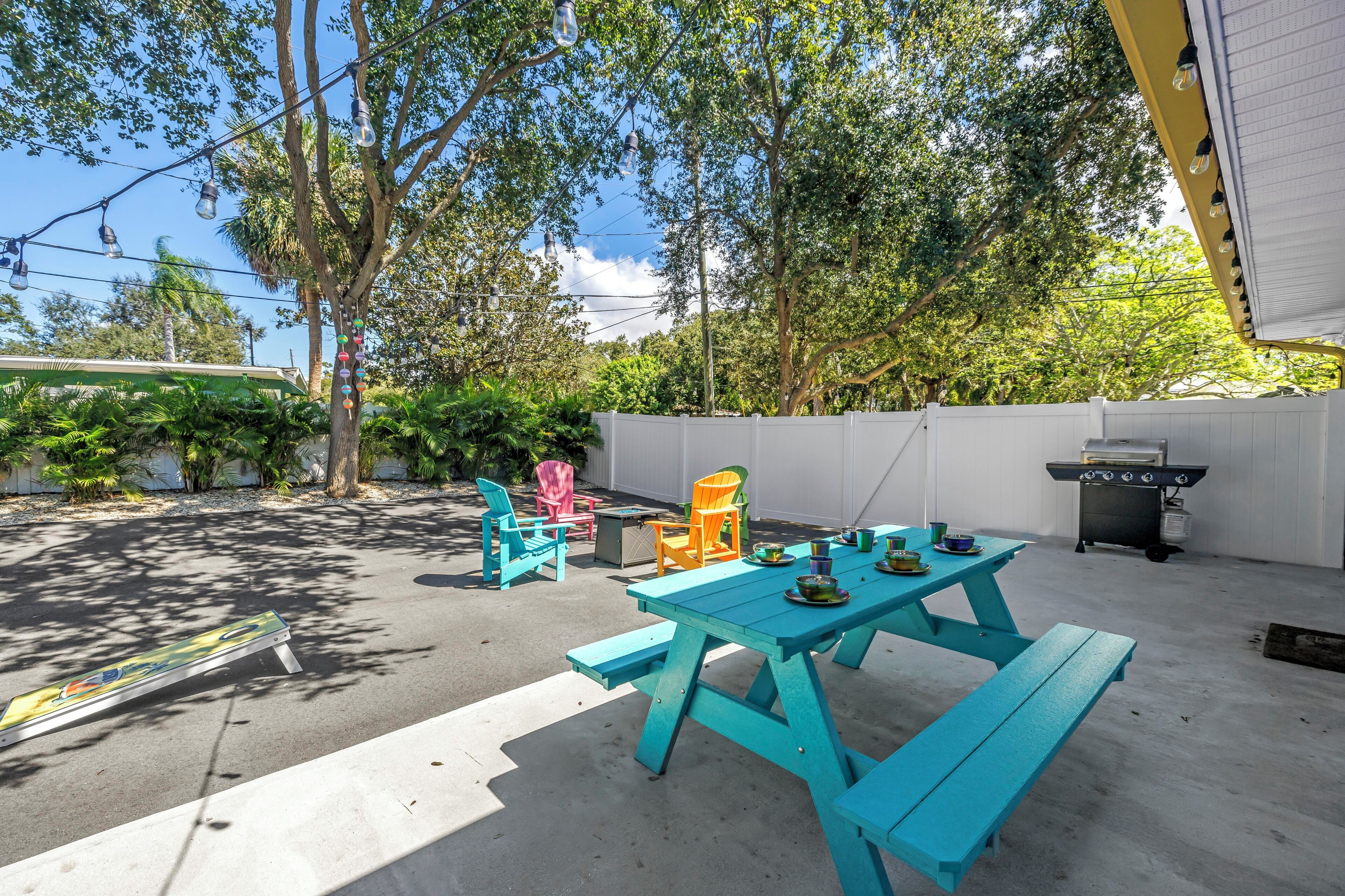 Une terrasse extérieure avec des tables et des chaises pour pique-nique, un barbecue et une clôture blanche.