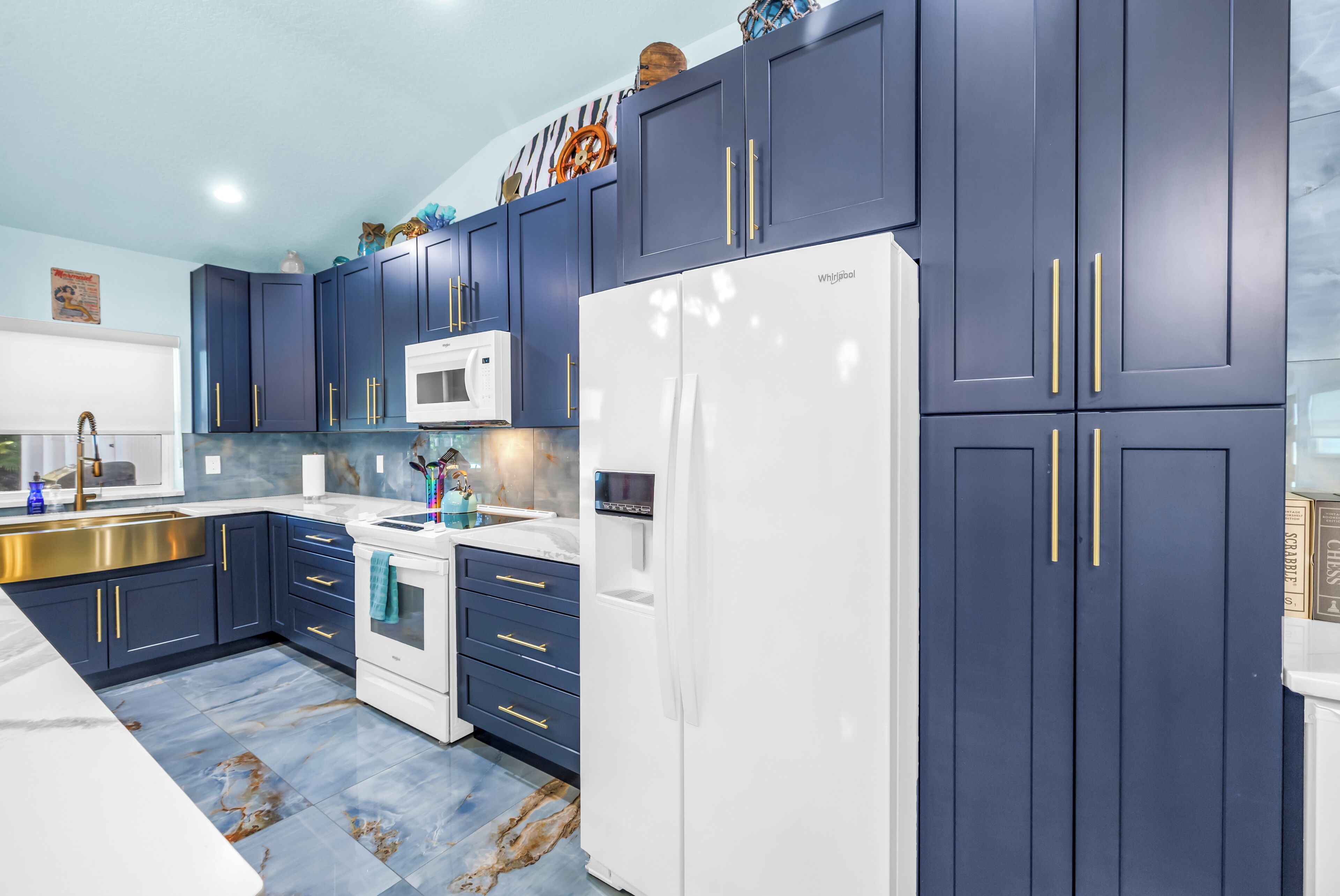 A modern kitchen with dark blue cabinets, a white refrigerator, and a stainless steel sink.