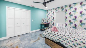Un dormitorio con paredes color esmeralda, una cama con estampado de peces de colores, un ventilador de techo, un armario y un espejo con papel tapiz de motivos marinos.