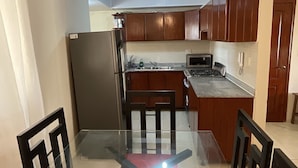 Una cocina con gabinetes de madera, un refrigerador de acero inoxidable, un microondas y una mesa de comedor de vidrio.