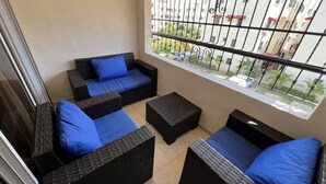 Un balcón con muebles de mimbre y vista a edificios cercanos.