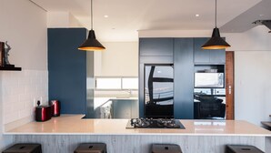 A modern kitchen with a central island, two pendant lights, and a view into the dining area. - The Bond Square - Two Bedroom Apartment, Sleeps 4 (Durban)