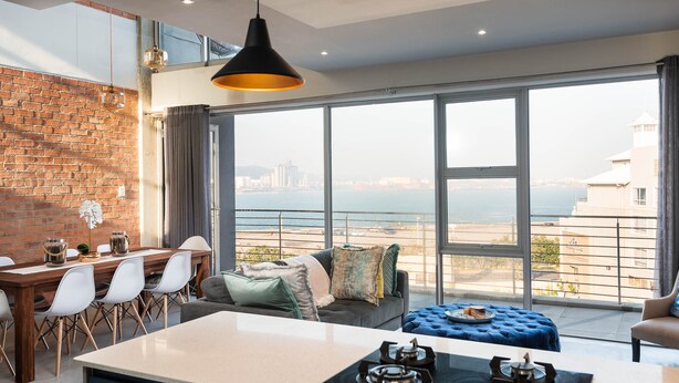 A modern living room with a large window, a dining area, and a kitchen. - The Bond Square - Two Bedroom Apartment, Sleeps 4 (Durban)