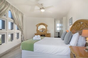 A hotel room with a bed, a ceiling fan, a wooden dresser, a mirror, and a window with curtains.