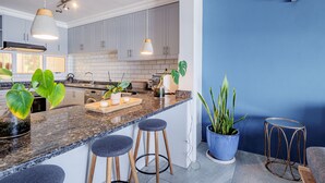 Una cocina moderna con encimeras de granito, taburetes de bar y plantas en macetas.