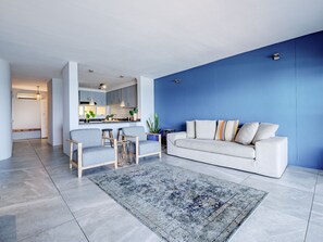 A modern living room with a sofa, chairs, a rug, and a kitchen in the background.