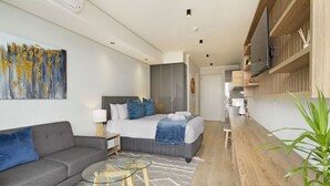 Une chambre d’hôtel moderne équipée d’un lit, d’un canapé, d’une table basse en verre, d’une télévision et d’une étagère en bois.