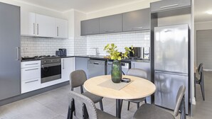 A modern kitchen with grey cabinets, a stainless steel refrigerator, and a dining table with chairs. - The Terraces 330 - One Bedroom Apartment, Sleeps 2 (Cape Town)