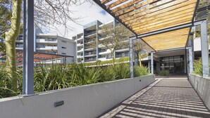 A covered walkway with a wooden ceiling, a white wall with a planter, and a building with multiple balconies in the background. - The Terraces 330 - One Bedroom Apartment, Sleeps 2 (Cape Town)
