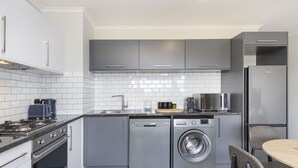 A modern kitchen with grey cabinets, a built-in dishwasher, a washing machine, a microwave, and a refrigerator. - The Terraces 330 - One Bedroom Apartment, Sleeps 2 (Cape Town)