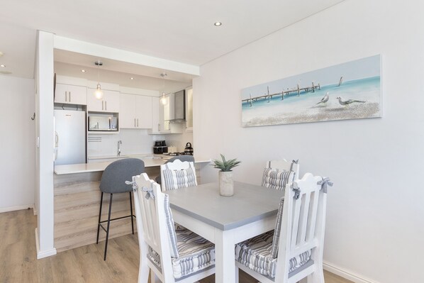 Una cocina moderna con armarios blancos y un comedor con sillas a rayas y una mesa gris.
