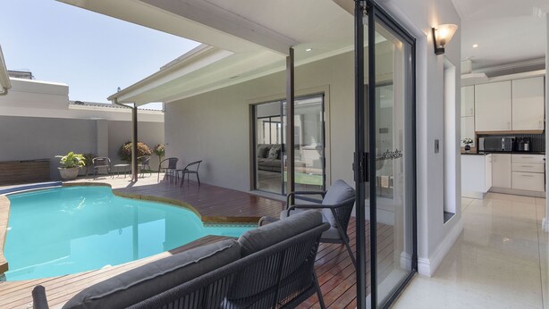 Una casa moderna con piscina, un patio con mobiliario exterior y una zona de cocina.