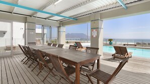 A wooden deck with a pool, lounge chairs, and a table with chairs. - Sea Spray B104 - Studio Apartment, Sleeps 2 (Cape Town)