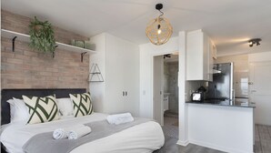 A modern hotel room with a bed, a small kitchen, and a bathroom. - Sea Spray B104 - Studio Apartment, Sleeps 2 (Cape Town)