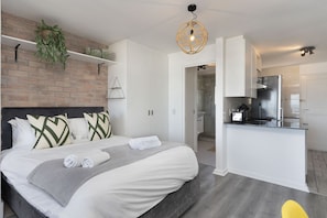 A modern hotel room with a bed, a kitchen area, and a shower. - Sea Spray B104 - Studio Apartment, Sleeps 2 (Cape Town)