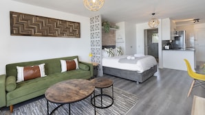 A modern living room with a green sofa, a bed, and a dining area with a yellow chair. - Sea Spray B104 - Studio Apartment, Sleeps 2 (Cape Town)