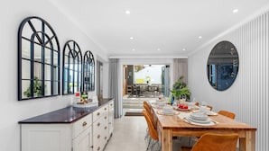 A modern dining area with a wooden table set for four, white cabinets, and a large mirror on the wall. - Rancho Relaxo - Five Bedroom House, Sleeps 10 (Cape Town)