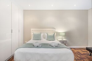 A neatly made bed with pillows, a bedside table with a lamp, and a bench.