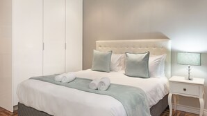 A neatly made bed with pillows and rolled towels, a bedside table with a lamp, and a wardrobe. - Sandringham 55 - Studio Apartment, Sleeps 2 (Cape Town)