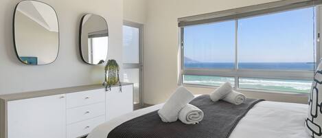 Un dormitorio moderno con una cama grande, un aparador, dos espejos y vista al océano.