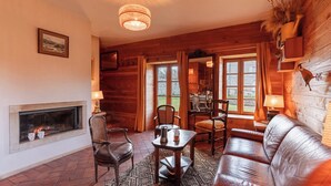 A cozy room with a fireplace, wooden walls, a leather sofa, and a dining table with chairs. - Pond, Forest, boat (Toury-sur-Jour)