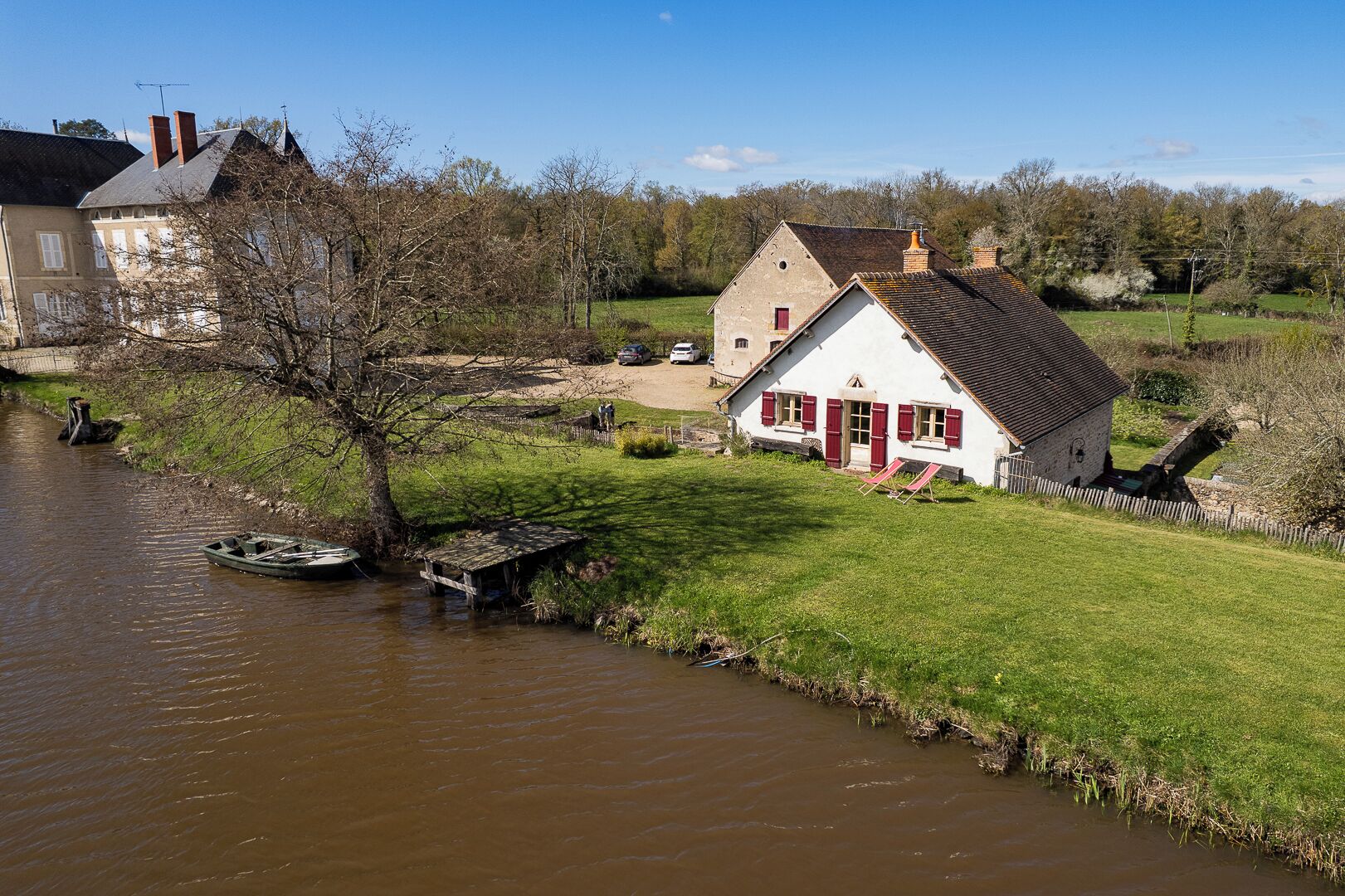 Een huis aan de rivier met een gazon, een klein steiger en een brug.