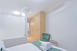 Une chambre à coucher avec un lit, un fauteuil vert, une armoire et une petite table sur laquelle se trouve un plateau.
