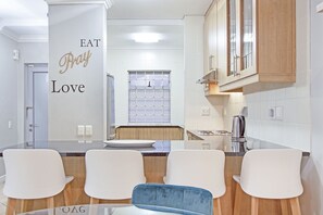 Een moderne keuken met een centraal eiland, witte stoelen en een muur met de tekst 'EAT Pray Love'.