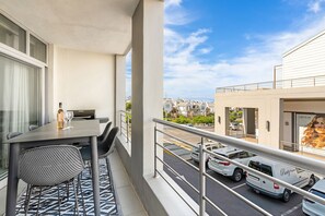 Un balcon avec une table, des chaises, une bouteille et un verre.
