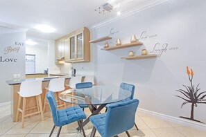 Une cuisine moderne avec un coin repas, comprenant une table en verre et des chaises bleues, ainsi que des œuvres d’art murales décoratives ornées de citations inspirantes.