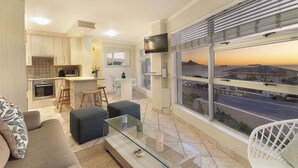 Una sala de estar moderna con una mesa de centro de vidrio, un sofá y vistas a un atardecer a través de amplias ventanas.