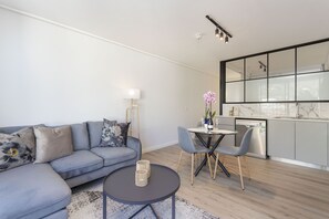 Una sala de estar moderna con un sofá gris, una mesa de centro redonda y un comedor con una pequeña mesa y sillas.