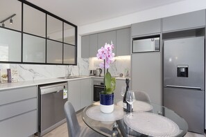 A modern kitchen with a built-in dishwasher, a refrigerator, a dining table with chairs, and a vase with flowers.