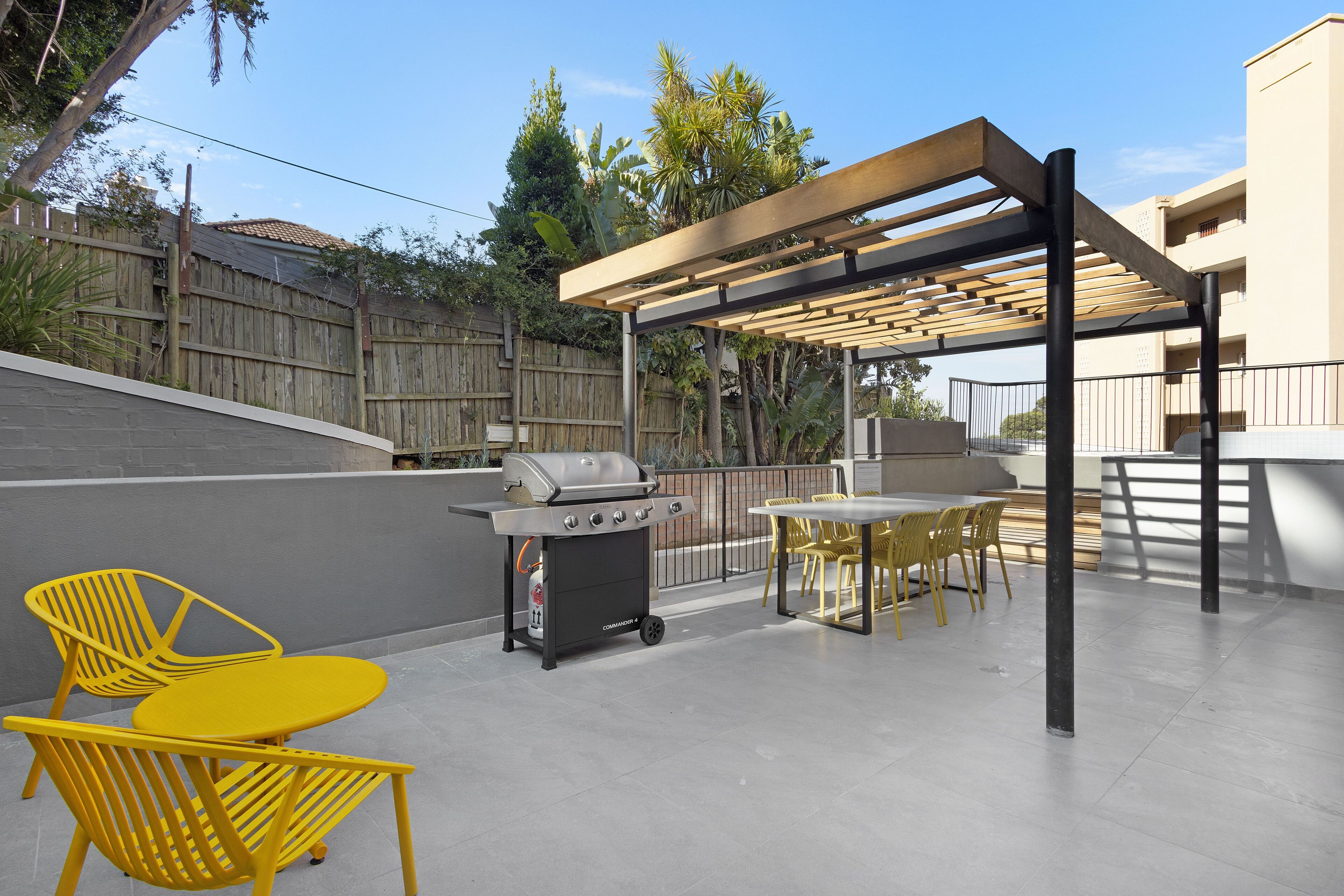 An outdoor patio with a grill, yellow chairs, and a pergola.