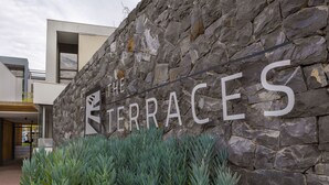 Eine Steinsäule mit dem Schriftzug "THE TERRACES" und ein modernes Gebäude im Hintergrund.