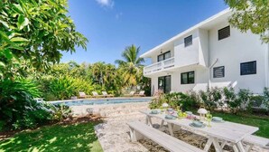 A modern house with a pool, outdoor dining area, and lush greenery. - Purple Palace -Fully Renovated w/Pool & Ocean View (Rincón)