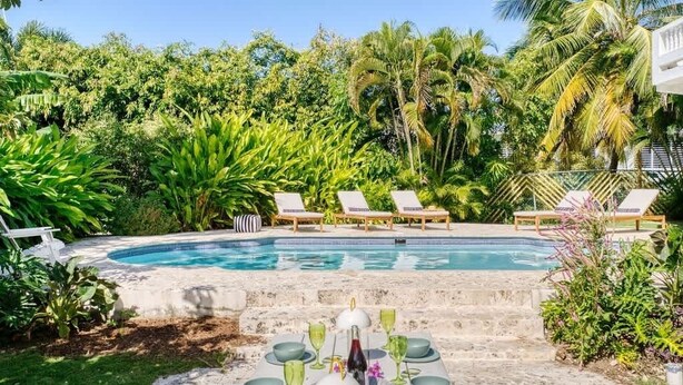 A poolside dining area with a table set for four, surrounded by lounge chairs and a swimming pool. - Purple Palace -Fully Renovated w/Pool & Ocean View (Rincón)