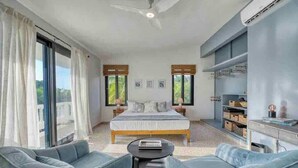 A modern bedroom with a large bed, a desk, and a seating area with two chairs. - Purple Palace -Fully Renovated w/Pool & Ocean View (Rincón)