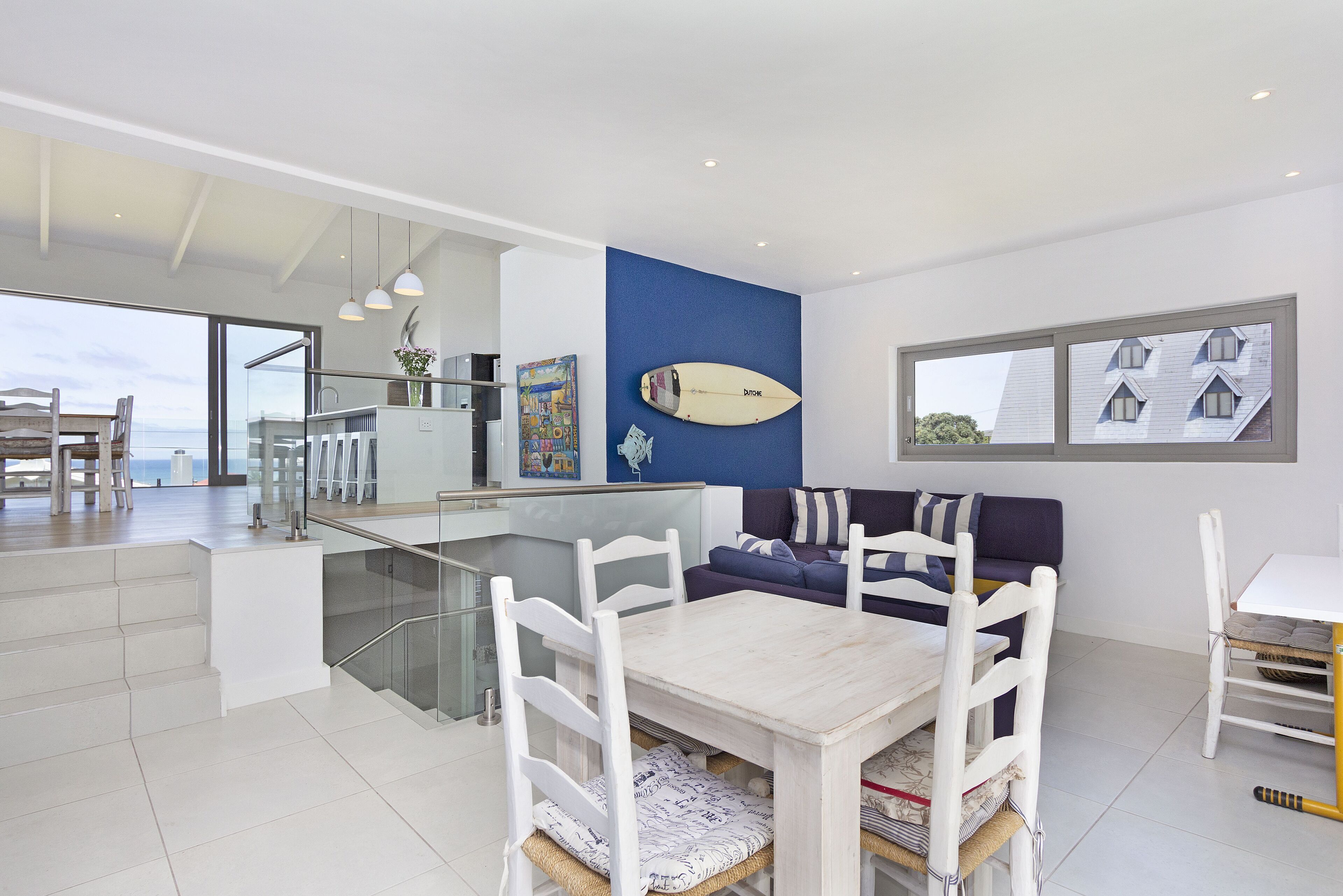 A modern kitchen with a dining area, a blue accent wall, and a surfboard decoration.