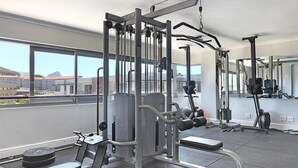 Ein Fitnessstudio mit verschiedenen Trainingsgeräten, großen Fenstern und Blick auf Gebäude und Berge.