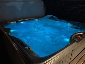 Ein Whirlpool mit blauer Beleuchtung, einer Steuerung mit rotem Knopf und einer ihn umgebenden Holzterrasse.