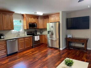 Una cocina moderna con armarios de madera, electrodomésticos de acero inoxidable y un televisor de pantalla plana grande.