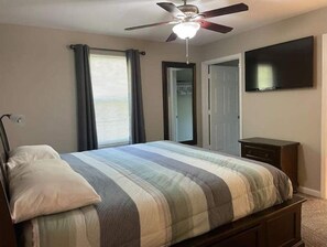 Ein Schlafzimmer mit Bett, Deckenventilator, an der Wand montiertem Fernseher und Kleiderschrank.