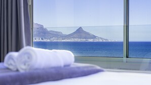 A hotel room with a large window overlooking a coastal city and a mountain. - Sea Spray B306 - Two Bedroom Apartment, Sleeps 4 (Cape Town)