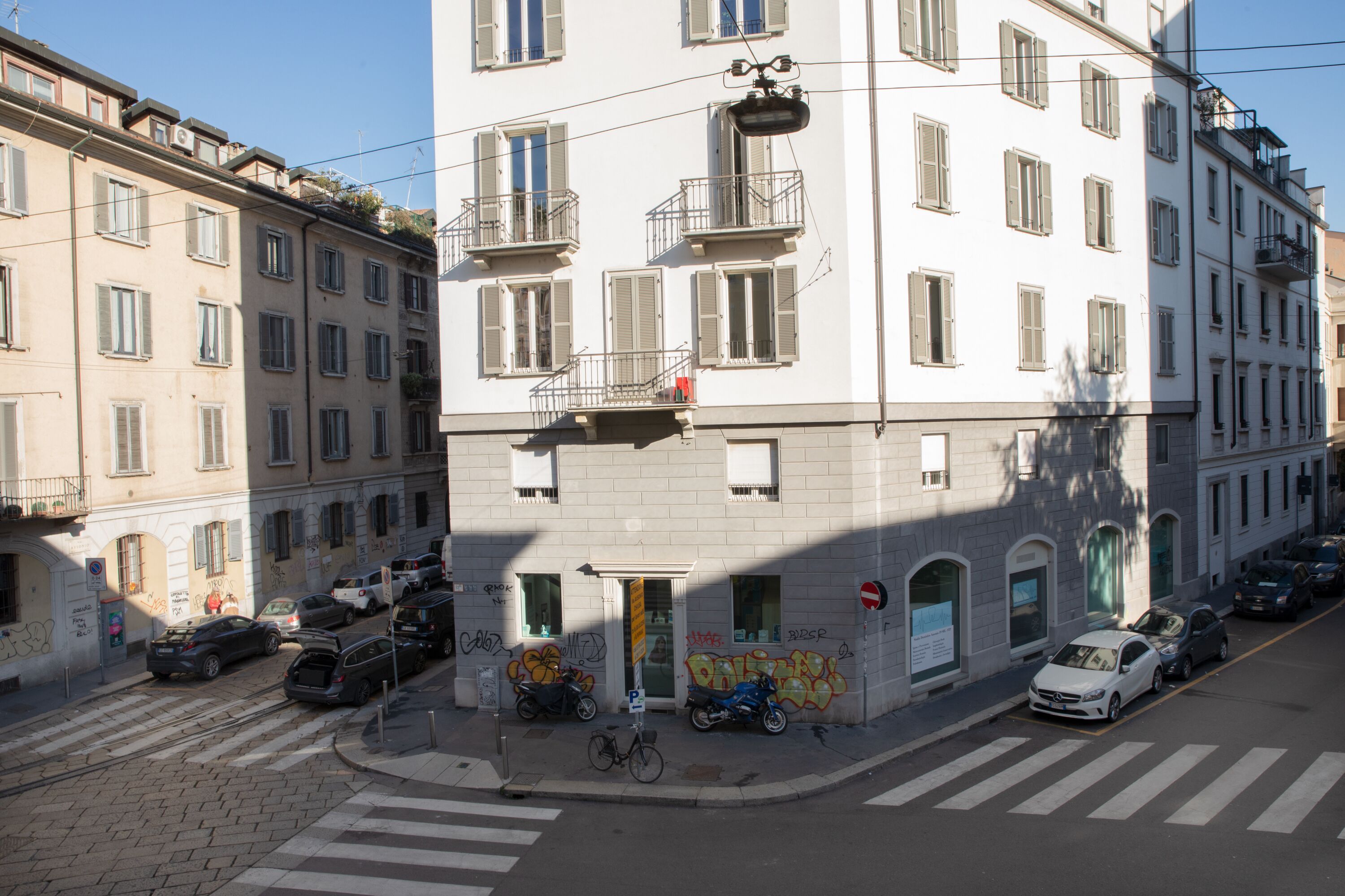 Un immeuble à plusieurs étages avec une entrée au rez-de-chaussée, un vélo garé devant et plusieurs voitures stationnées dans la rue.