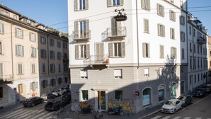 En bygning med flere etager og en indgang i stueplan, en cykel parkeret foran og flere biler på gaden.